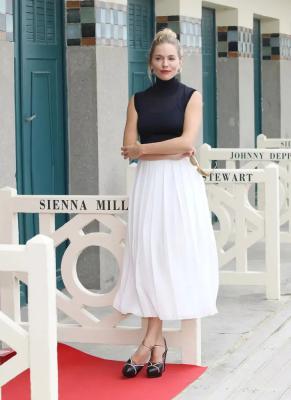 Сиенна Миллер в белой плиссированной юбке миди, черном топе и туфлях на платформе