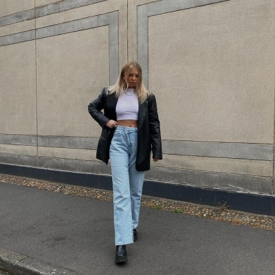 Девушка в прямых джинсах с асимметричной талией, кожаном пиджаке и топе